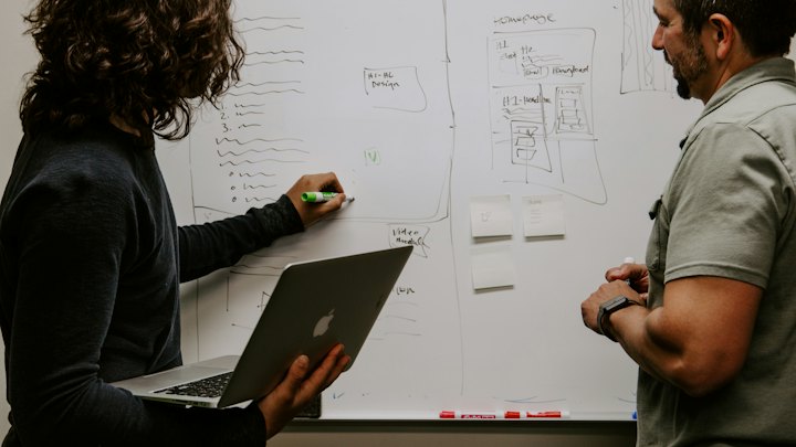 Two colleagues mapping out a plan on a whiteboard